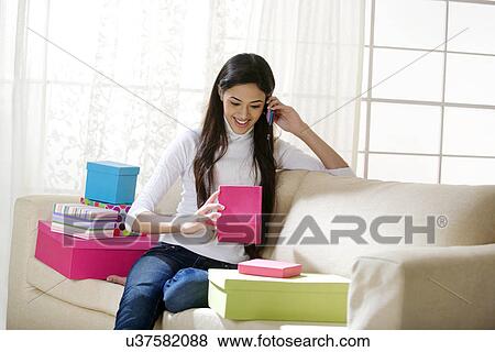 Stock Photo - Young woman talking on a mobile phone while looking at a gift box . Fotosearch