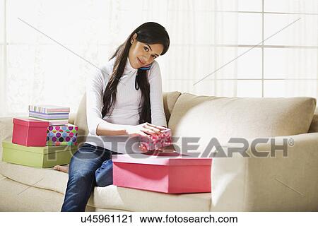 Stock Image - Young woman with a mobile phone holding a gift . Fotosearch
