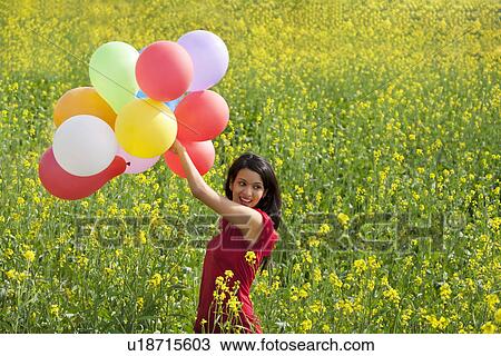 Stock Image - Young woman with balloons in a field . Fotosearch