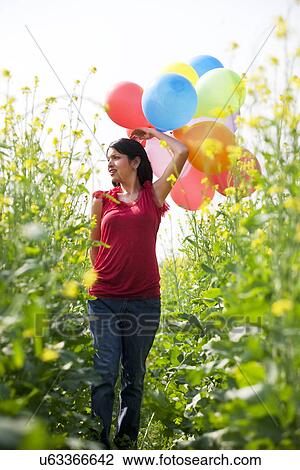 Stock Image - Young woman with balloons walking in a field . Fotosearch