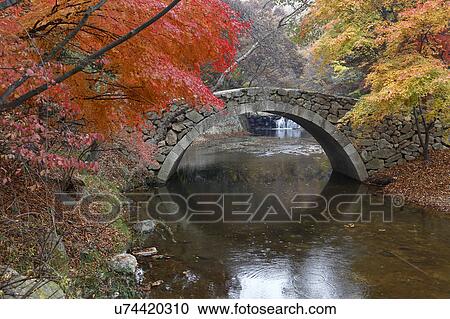 Stock Image - Autumn color and old stone arched bridge at Namsangol traditional folk village, Seoul, South Korea. Fotosearch