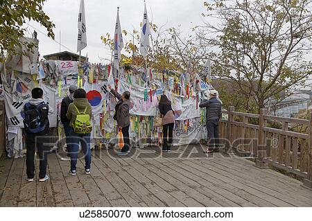Stock Image - Barbed wire fence separates South from North Korea - South Korean flags and prayer wishes attached to fence for those separated or who had died during the Korean War. Fotosearch