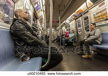 Stock Image - Man on train rides New York City Subway late at night. Fotosearch