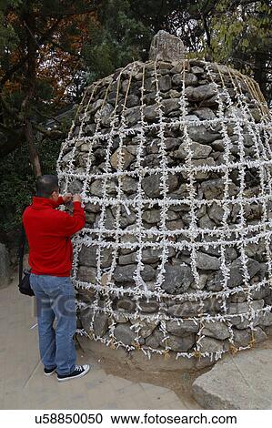 Stock Image - Man places wish at sacred "wish stones" at Namsangol traditional folk village, Seoul, South Korea. Fotosearch