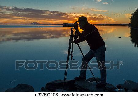 Stock Photograph - Silhouette of Photographer shooting Mt Redoubt Volcano at Skilak Lake, Alaska. Fotosearch