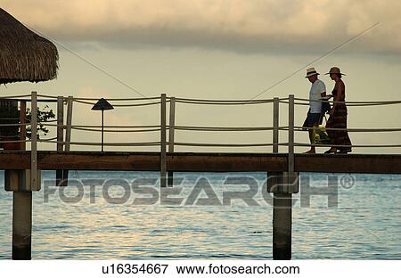 Stock Photo - A mid adult couple walking on a pier, Moorea, Tahiti, French Polynesia, South Pacific. Fotosearch