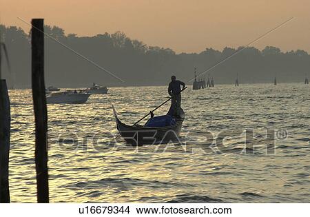 Picture - Oarsmen driving a gondola during sunset in Venice, Italy. Fotosearch