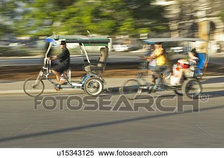 Stock Photography - Bicycle taxis speeding through the streets with sunlight on it in Havana. Fotosearch