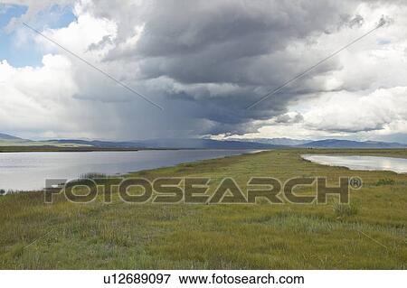 Stock Photo - Storm clouds over grasslands and mountains. Fotosearch