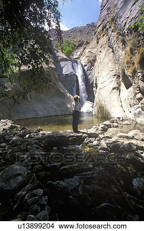 Woman in hat in Tahquitz Canyon looks at waterfall in Palm Springs View Large Photo Image Picture - Woman in hat in Tahquitz Canyon looks at waterfall in Palm Springs. Fotosearch