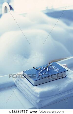 Stock Photo - Fresh Towels, a Book andGlasses Next to a Bubble Bath, High Angle View, Differential Focus. Fotosearch