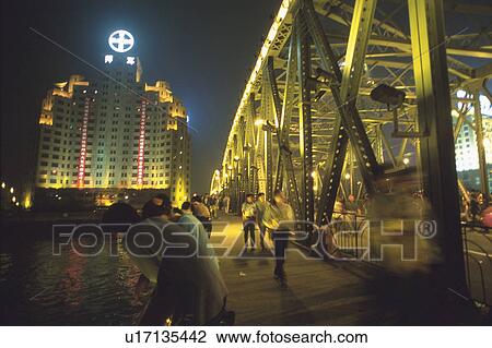 Stock Image -  Several Tourists at Shanghai Bay, Looking at the Ocean, Surrounded By Illuminated Buildings, Side View, Shanghai, China. Fotosearch