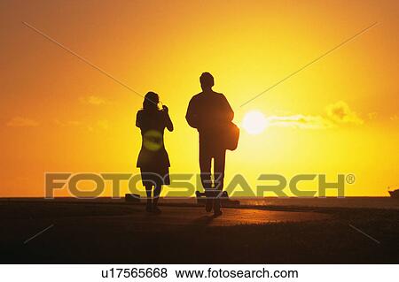 Stock Photo -  a Couple Walking By Sunset, Hawaii, USA, Rear View, Lens Flare. Fotosearch
