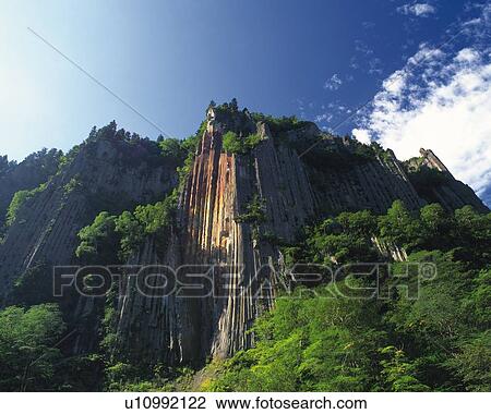 Stock Image -  a Huge Cliff Overgrown With Some Trees, Under a Blue Sky, Low Angle View, Hokkaido Prefecture, Japan. Fotosearch