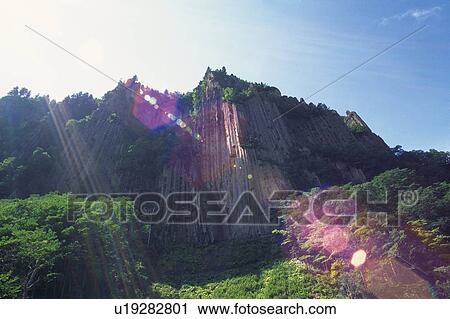 Stock Image -  a Large Cliff, Surrounded By Trees and Bushes By Sounkyo, Low Angle View, Lens Flare, Hokkaido Prefecture, Japan. Fotosearch