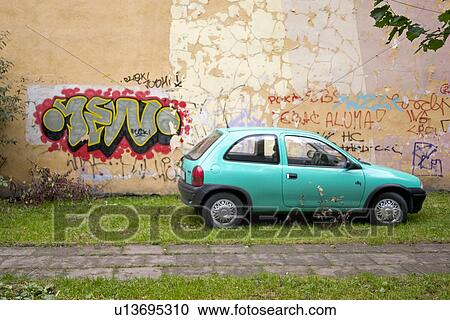 Stock Image - Graffiti on wall of building next to a turquoise car. Fotosearch
