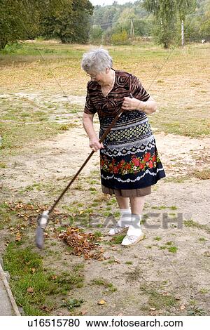 Stock Image - Great grandmother raking leaves, Zawady, Central Poland. Fotosearch