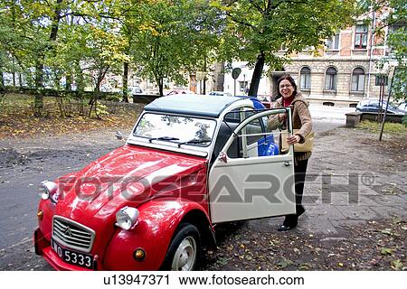 Stock Image - Owner stepping into beautiful red white and blue French Peugeot car. Fotosearch