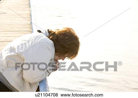 Stock Photo - Woman on a dock looking into the lake. Fotosearch