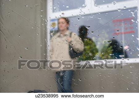 Stock Photography - Woman waiting outside at grocery store with rain on car window, Rzeczyca, Central Poland. Fotosearch