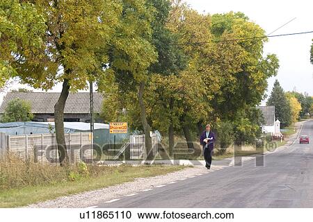 Stock Image - Woman walking along the road, Rawa Mazowiecka, Central Poland. Fotosearch