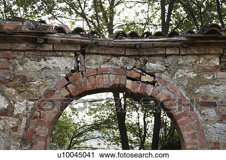 Stock Image - Dilapidated stone archway with trees in background in Tuscany, Italy.. Fotosearch