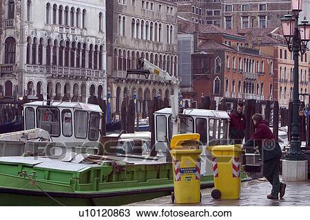 Stock Image - Garbage barges moored at side of Grand Canal with men loading yellow garbage containers. Fotosearch