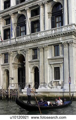 Stock Image - Gondolier in Gondola with passengers on Grande Canal - Palazzo in background. Fotosearch
