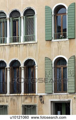 Stock Image - green shuttered arched windows on light yellow beige building. Fotosearch