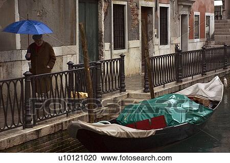 Man with umbrella walking beside canal in rain View Large Photo Image Stock Image - Man with umbrella walking beside canal in rain. Fotosearch