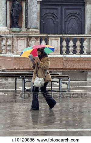 Stock Photograph - Tourist reading guide and walking under umbrella. Fotosearch