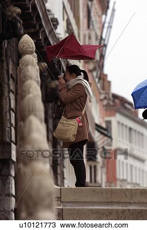 Stock Image - Windblown tourist taking photograph with red umbrella. Fotosearch