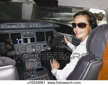 Stock Image - Female pilot in cockpit of private jet.. Fotosearch