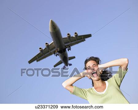 Woman covering ears and screaming with plane flying overhead. View Large Photo Image Stock Photo - Woman covering ears and screaming with plane flying overhead.. Fotosearch