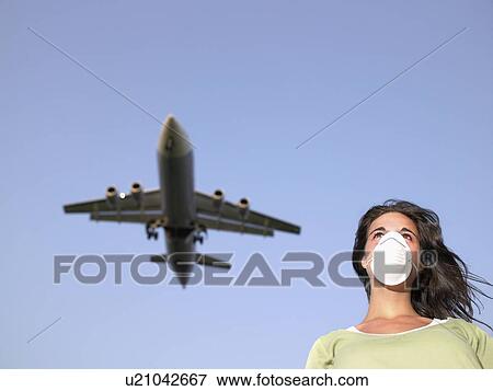 Woman wearing a surgical mask while a plane flies overhead. View Large Photo Image Stock Photo - Woman wearing a surgical mask while a plane flies overhead.. Fotosearch