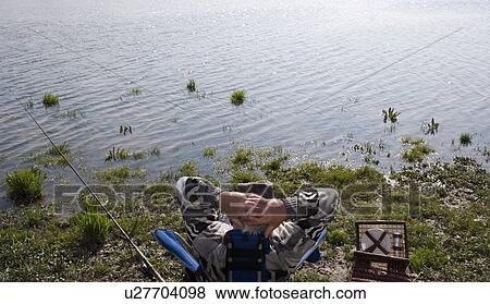 Senior man fishing by river, sitting with hands behind head, rear view View Large Photo Image Stock Photo - Senior man fishing by river, sitting with hands behind head, rear view. Fotosearch