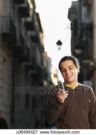 Stock Photo - Teenage boy (16-18) using mobile phone in street, smiling. Fotosearch