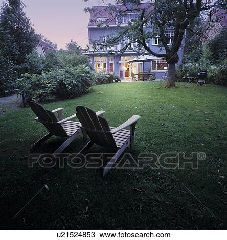 Stock Image - Two lawn chairs sitting on a lawn with a large house in the background.. Fotosearch