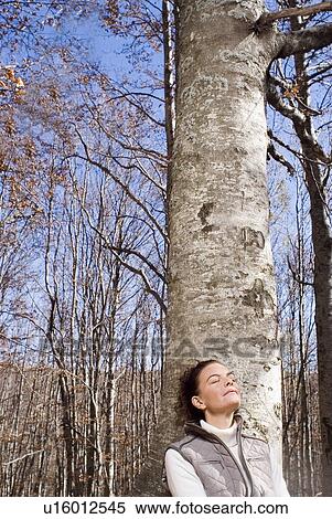 Stock Photography - Woman leaning against a tree smiling.. Fotosearch