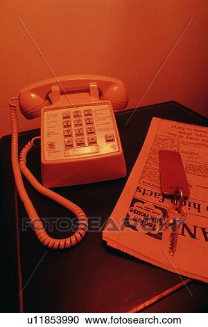 Stock Image - Telephone, Room Key and Newspaper on Desk, High Angle View, Toned Image. Fotosearch