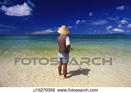 Stock Photograph - An Angler of the Tropical Beach, Rear View. Fotosearch