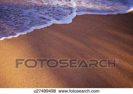 Stock Photo - Gentle Waves Against the Sandy Beach, High Angle View. Fotosearch
