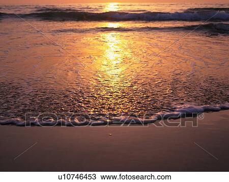 Stock Image - Lapping Waves of a Sunset Beach, High Angle View. Fotosearch