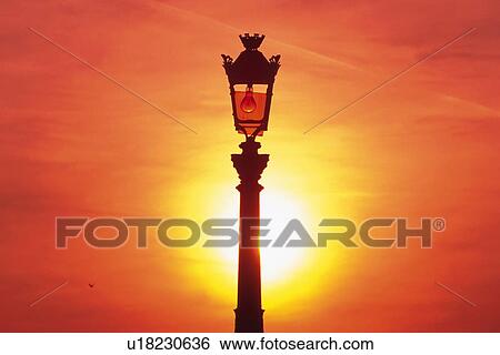 Stock Photograph - Closed Up Image of a Street Lamp By Sunset, the Sun Visible in the Background, Front View, Paris, France. Fotosearch