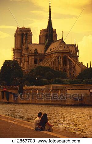 Stock Image - Image of a Couple Sitting by the Seine, Looking at the Notre Dame de Paris Cathedral, Side View, Paris, France. Fotosearch