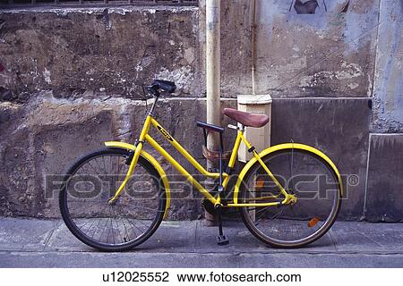 Stock Image - Image of a Yellow Bicycle Standing Near a Stone Wall, Side View, Paris, France. Fotosearch