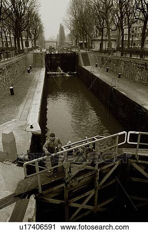 Stock Image - Closed Up Image of a Little River in Paris, a Man Standing on a Little Bridge Over it, High Angle View, Paris, France. Fotosearch