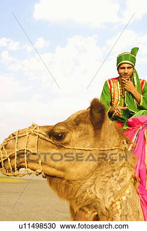 Stock Image - Low angle view of a young man riding a camel. Fotosearch