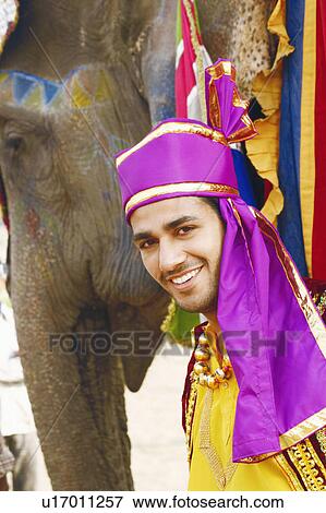 Stock Photo - Portrait of a young man standing with an elephant. Fotosearch