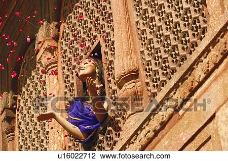 Stock Image - Low angle view of a young woman throwing rose petal from a window, Agra Fort, Agra, Uttar Pradesh, India. Fotosearch